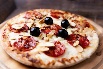 Pizza with salami and mozzarella cheese. Wooden background. Soft focus. Close up.