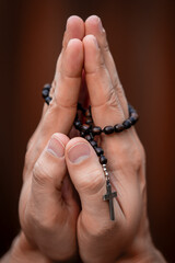 Praying hands of a man with a Christian cross and rosary