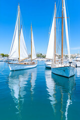 Obraz premium Classic sailboats anchored in a calm, clear harbor reflecting sunlight
