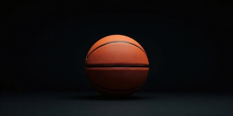 Obraz premium A solitary basketball rests on a dark surface, illuminated against a black background, ready for the next game.