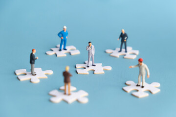 Miniature people standing on jigsaw puzzles. Concept of work collaboration