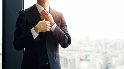 Male business person adjusting his tie in the office with the city in the background