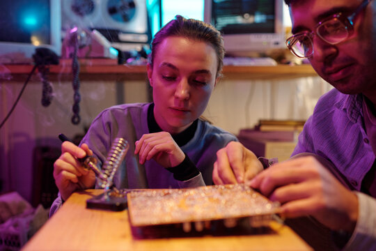 Two diverse young people repairing old computer detail, using soldering iron, closeup shot