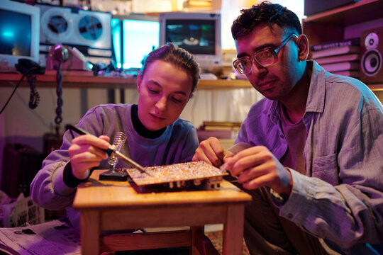 Two diverse young people repairing old computer circuit board , using soldering iron, medium shot