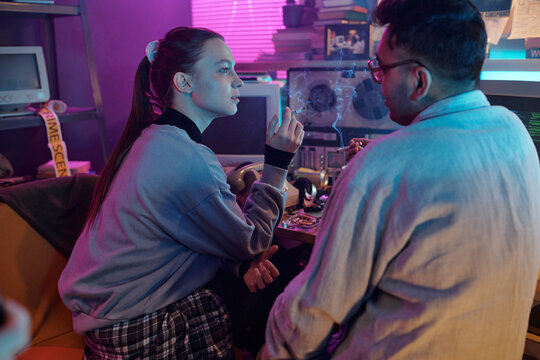 Young woman speaking with male colleague while they smoking during break, vintage computer displaying running programming code in background