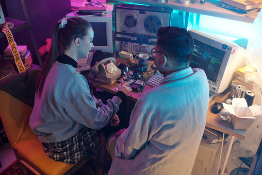 Two diverse young programmers chatting and smoking while sitting at wooden desk with vintage computer monitors devices on it