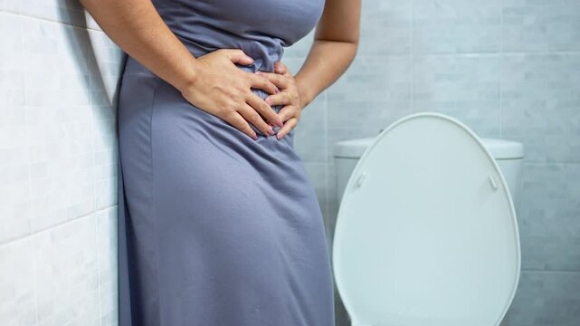 woman standing in the toilet holding her lower belly in pain, suffering from stomach cramps and discomfort due to menstrual period, pms, or digestive issues like diarrhea