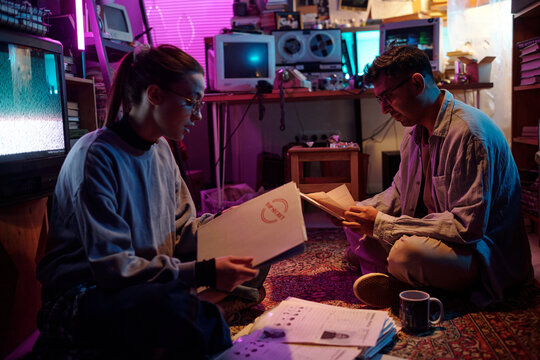 Two young investigators examining white folders labeled top secret and opening them while working together sitting on floor