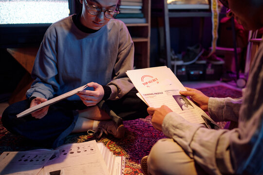 Young people examining white folders labeled top secret and opening them while working together sitting on floor