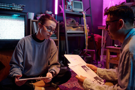Young hackers looking through criminal profiles working on secret project when sitting on carpet with two piles of papers