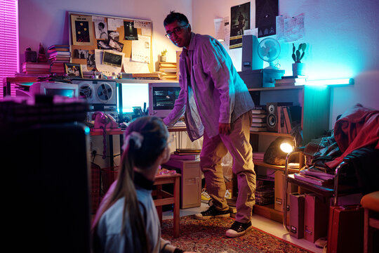 Young woman sitting on floor talking to her male colleague standing in background in cluttered room