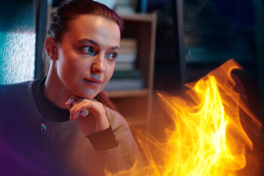 Portrait of thoughtful Caucasian girl sitting in cluttered room with unusual fire-like light effect in foreground