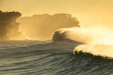 Large waves crash along Sydney’s rocky coastline at sunrise.
