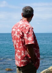 Hombre de mediana edad en la playa con camisa hawaiana mirando el mar 
