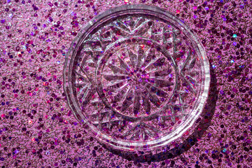 Full frame macro abstract texture background of a crystal glass coaster on sparkling multicolor pink glitter with copy space
