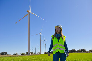 Female engineer walking in wind turbine field holding tablet