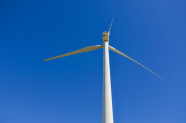 Fototapeta premium Wind turbine generating renewable energy against blue sky