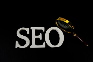 Seo words (Search Engine Optimization) letters with magnifying glass on black background