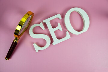 Seo words (Search Engine Optimization) letters with magnifying glass on pink background