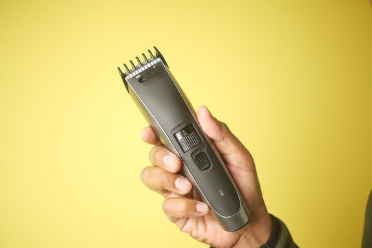 Hand holding hair clipper against a bright yellow backdrop