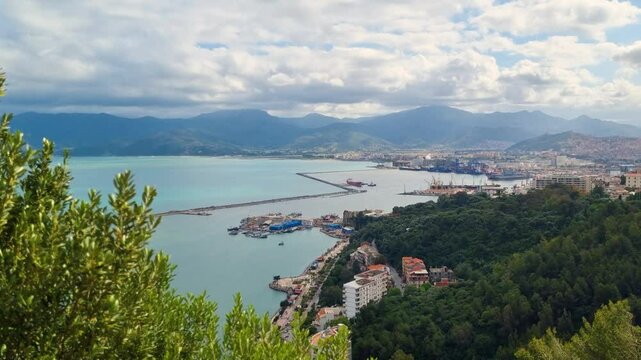 Panoramic view of the North African town of Bejaia, Algeria, on a cloudy day, showcasing the harbor, city center, the Kabylie Mountains, and the Mediterranean Sea in the background