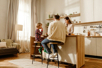 A school-aged European boy with short blond hair, having breakfast with his mid-30s parents in...