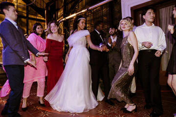 Fototapeta premium A young Black bride in her late 20s, dancing with her young Black groom in the middle of the dance floor, among the wedding guests, in a spacious hall, all having fun and smiling
