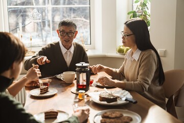 An elderly Asian grandpa in his late 70s, talking to his family as he sits at the dinner table, having breakfast with them in the morning, with his middle-aged daughter sitting beside him