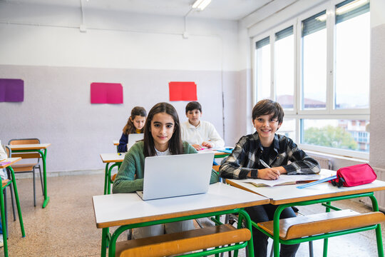 Elementary school students learning in classroom with laptop and notebook