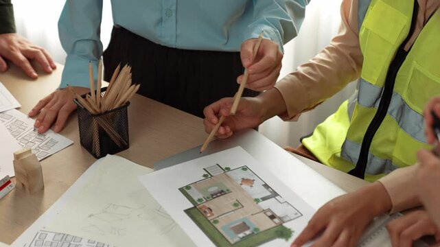 Smart architect and safety engineer discussion about building blueprint on table with architectural document, measurement tools and wooden block scatter around at modern office. Closeup. Delineation.