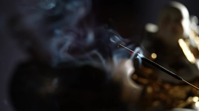 Asian incense stick in stick holder burning with smoke on dark background, close up. Meditation, yoga, self development and sound therapy concept