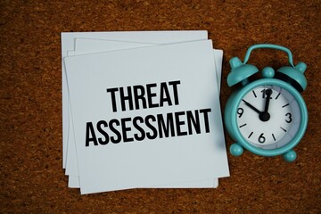 Threat Assessment text on sticky note with alarm clock on cork paper background