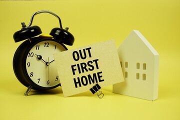 Our First Home text with house model and alarm clock on yellow background