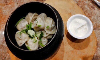 Dumplings in pot with herbs and sour cream. Hearty meal in close-up. National traditional Russian dish. Pelmeni with fresh green onions