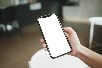 Hand holding a smartphone with a blank white screen in a modern indoor setting, capturing a casual moment of digital connectivity.