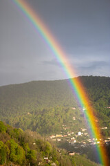 Vivid Rainbow Spanning Over Forested Hills and Rural Village Homes