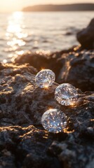 Three clear glass spheres rest on dark rocks near the ocean at sunset, reflecting the golden light.