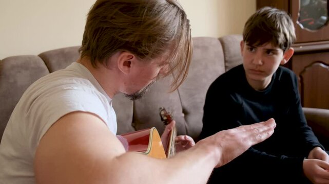 Young handsome music teacher giving a lesson to a teenage boy teaching the young man to play an acoustic six-string guitar. Music education for teenagers.