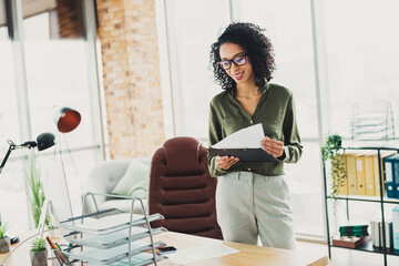 Smiling businesswoman working in a modern office environment, reading documents and displaying...