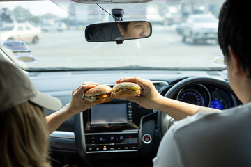Naklejka premium Couple is sharing a hamburger while traveling in a car