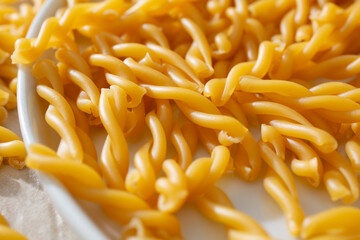 A closeup view of a pile of gluten-free gemelli pasta spilling over a plate.