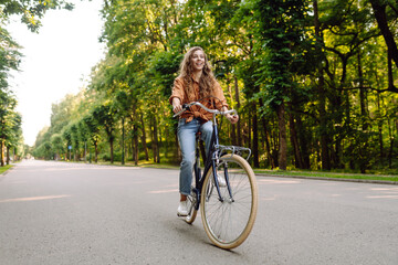 Young beautiful woman riding a bicycle in a sunny park. Tourist having fun in the park, enjoying a walk. Concept of recreation, walks. Active lifestyle.