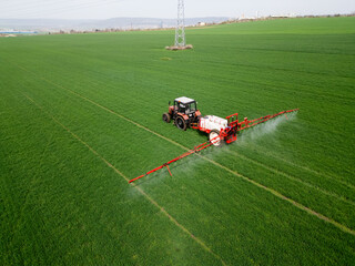 Tractor spraying fertilizer or pesticide on a large green field during spring, demonstrating modern agricultural technology and crop care