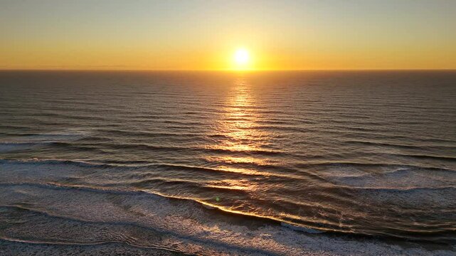 Drone captures smooth flight over ocean during golden sunset, with calm waves and sun reflecting off water in a quiet, open seascape filled with warmth and tranquility.