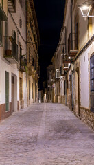 A narrow, cobblestone street at night with a few buildings on either side. Streets of Baeza, Spain, by night