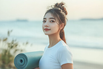 Beautiful chinese woman in her 30s standing with yoga mat near the ocean sea and smiling