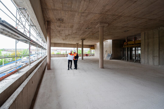 Architect and engineer inspecting a shell construction site with blueprints.
