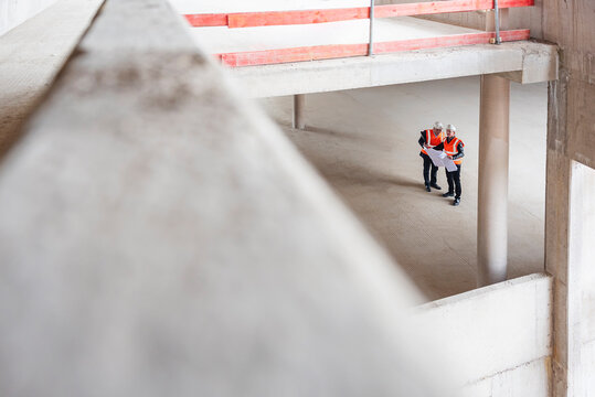 Two engineers inspecting a shell construction site with blueprints.