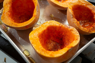 A view of a tray of seasoned honeynut squash, prepared for baking.