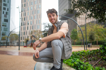 Young man smiling and crouching in a city park